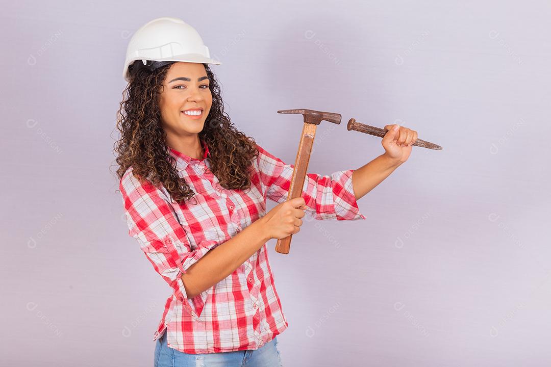 Mulher de empreiteiro segurando um martelo sorrindo sobre fundo branco.