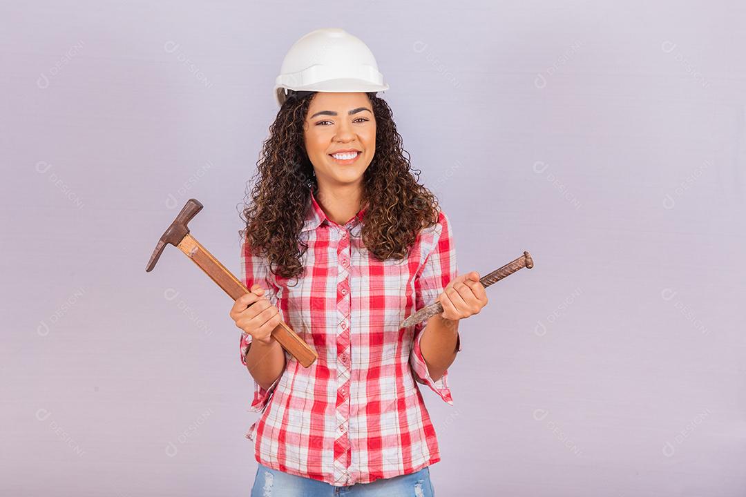 Mulher de empreiteiro segurando um martelo sorrindo sobre fundo branco.