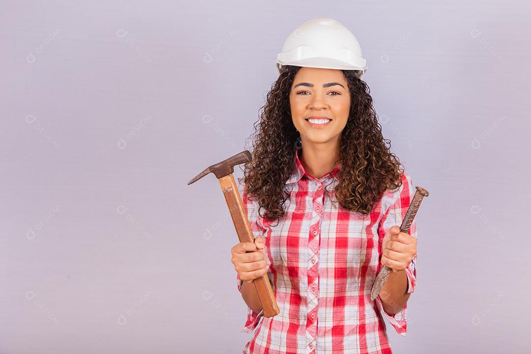 Mulher de empreiteiro segurando um martelo sorrindo sobre fundo branco.