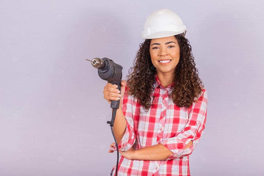 mulher afro segurando uma furadeira elétrica em fundo branco.