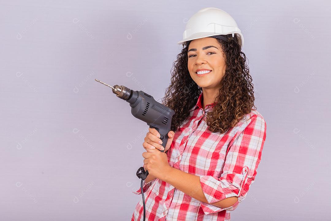 mulher afro segurando uma furadeira elétrica em fundo branco.