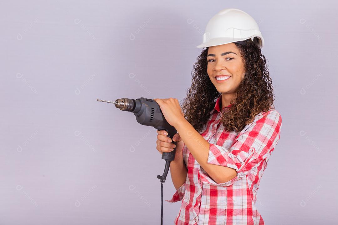 mulher afro segurando uma furadeira elétrica em fundo branco.