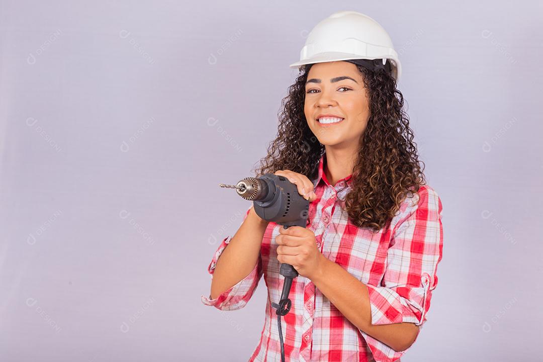 mulher afro segurando uma furadeira elétrica em fundo branco.