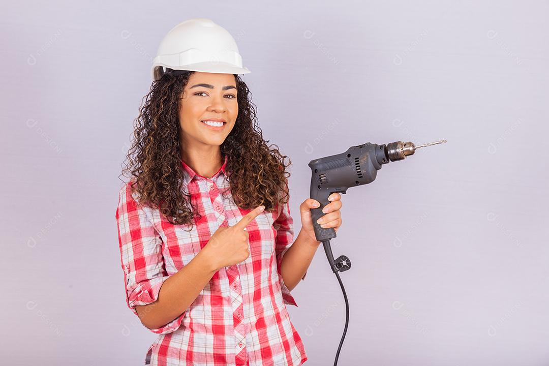 mulher afro segurando uma furadeira elétrica em fundo branco.