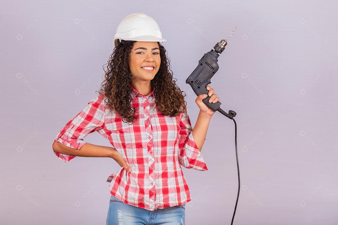 mulher afro segurando uma furadeira elétrica em fundo branco.