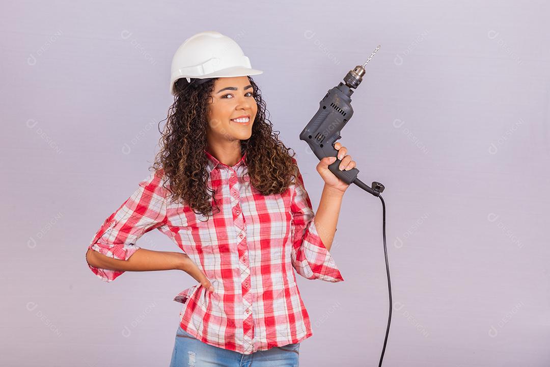 mulher afro segurando uma furadeira elétrica em fundo branco.