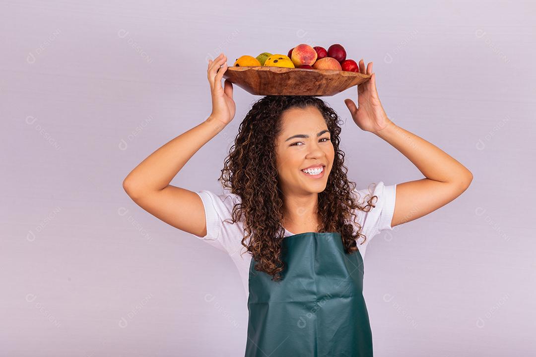 menina afro sorridente com cesta de frutas na cabeça sorrindo para a câmera