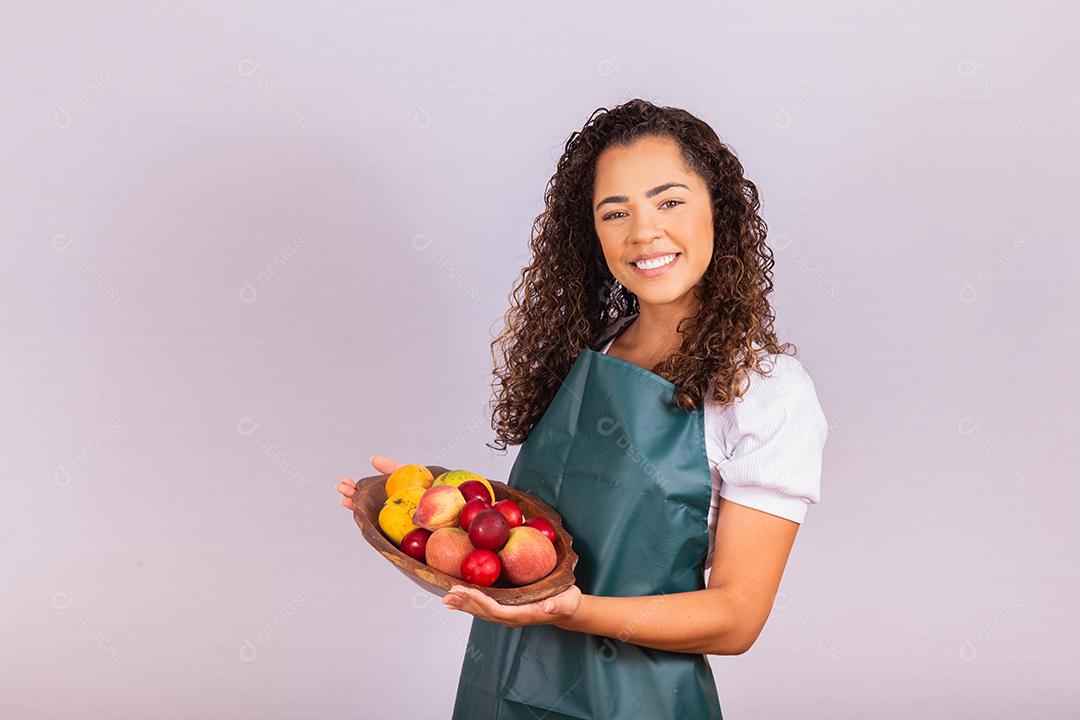 mulher jovem agricultor segurando uma tigela com frutas. Manga, pêssego e maçã na cesta na mão da menina