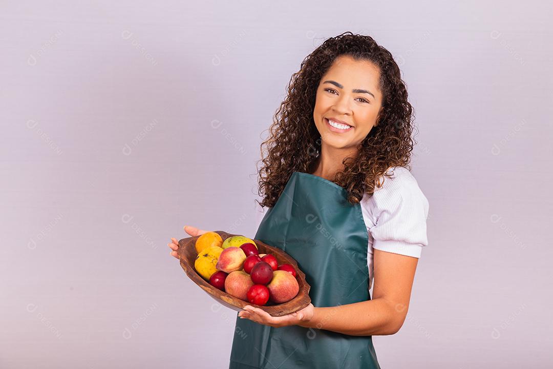 mulher jovem agricultor segurando uma tigela com frutas. Manga, pêssego e maçã na cesta na mão da menina