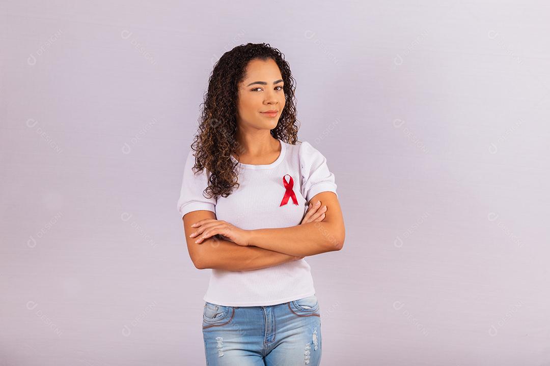 Jovem mulher com laço vermelho na camiseta para campanha de prevenção do HIV. Braços cruzados
