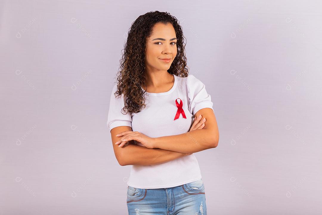 Jovem mulher com laço vermelho na camiseta para campanha de prevenção do HIV. Braços cruzados