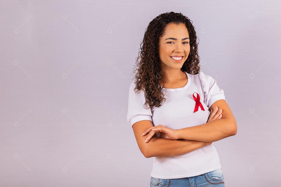 Jovem mulher com laço vermelho na camiseta para campanha de prevenção do HIV. Braços cruzados