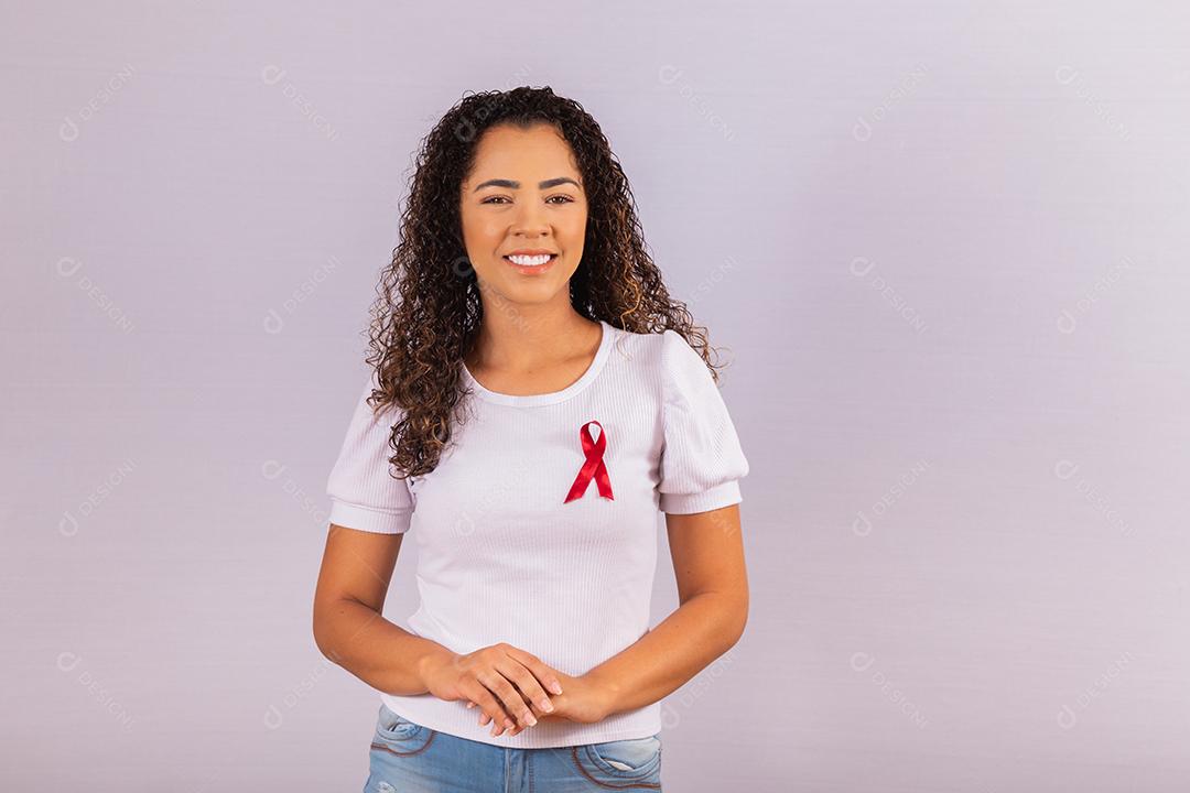 Jovem mulher com laço vermelho na camiseta para campanha de prevenção do HIV. Braços cruzados