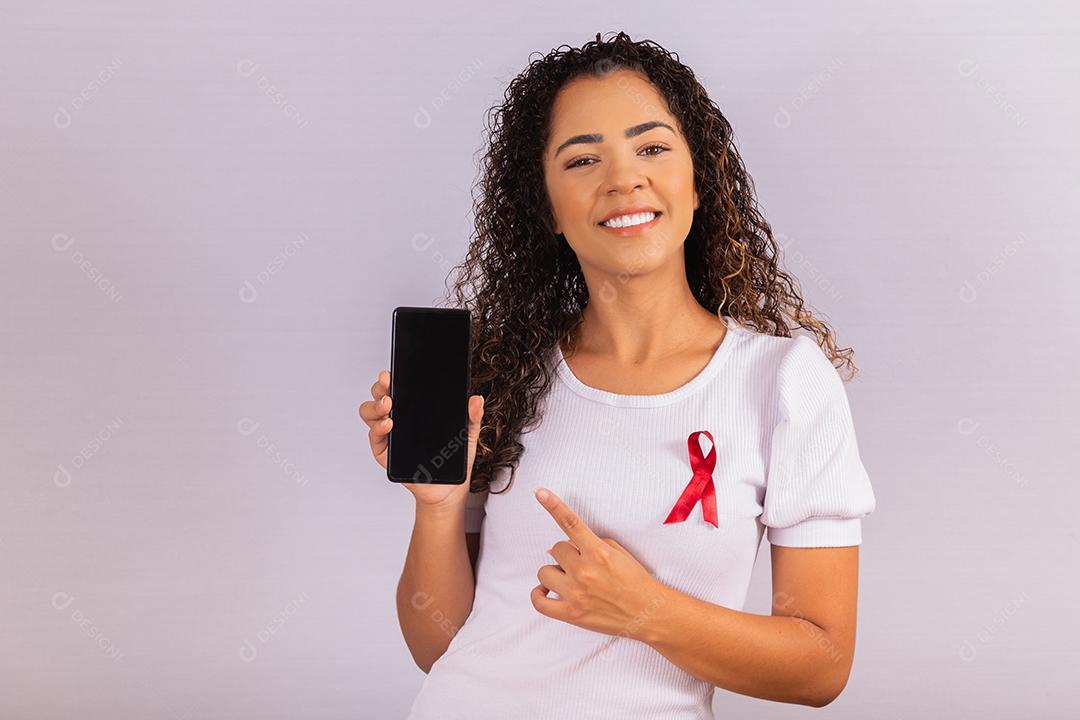 O conceito do Dia Mundial da AIDS. Jovem segura smartphone com tela em branco e fita vermelha na camiseta