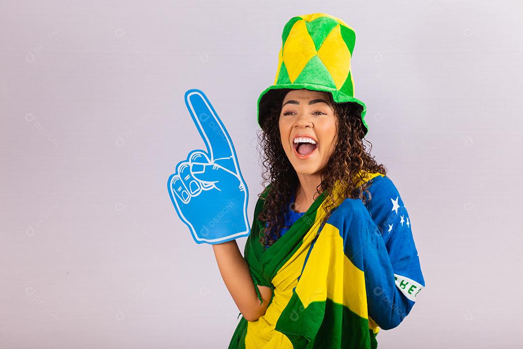 Mulher afro olhando para a câmera segurando a luva de futebol com roupa brasileira.