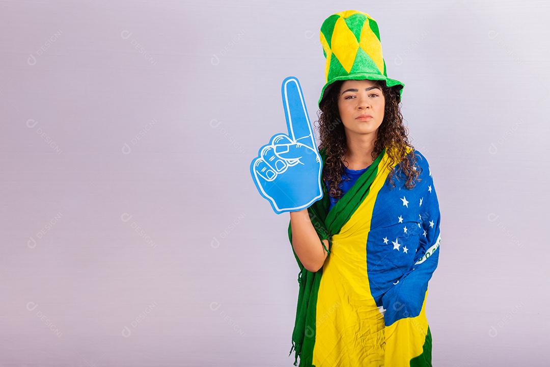 Mulher afro olhando para a câmera segurando a luva de futebol com roupa brasileira.