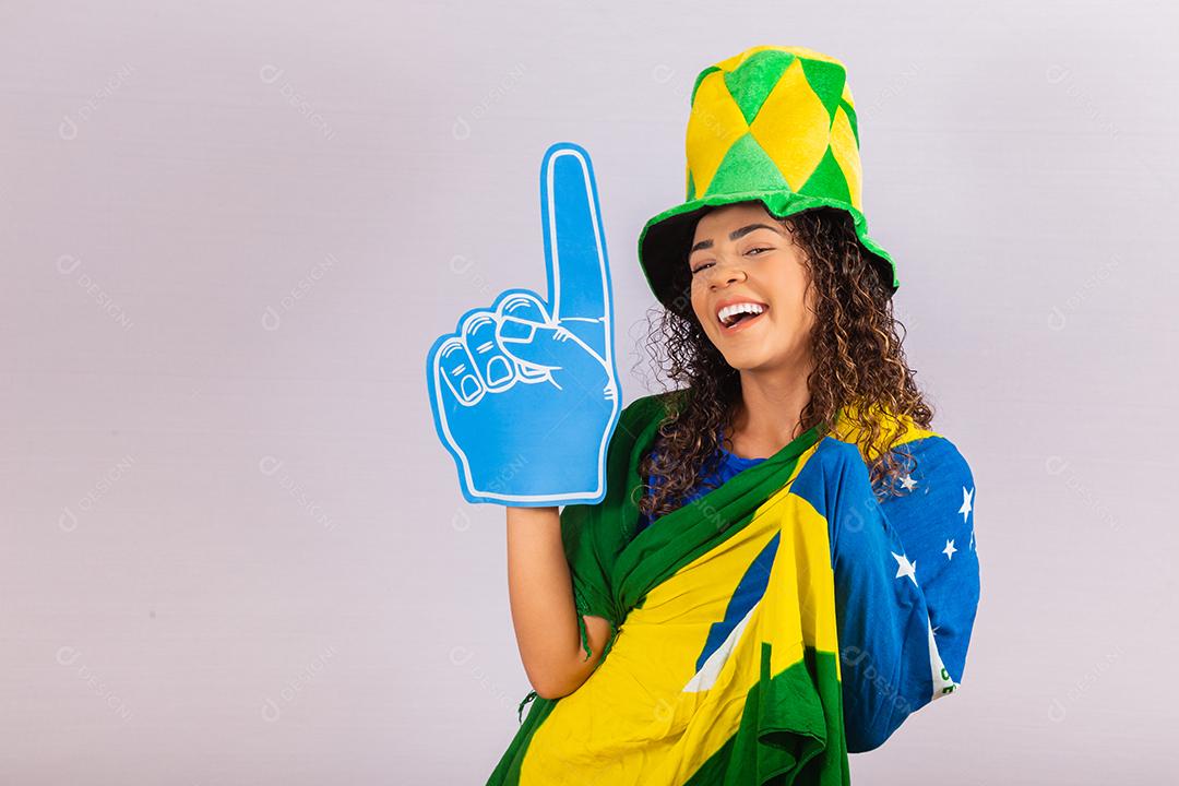 Mulher afro olhando para a câmera segurando a luva de futebol com roupa brasileira.