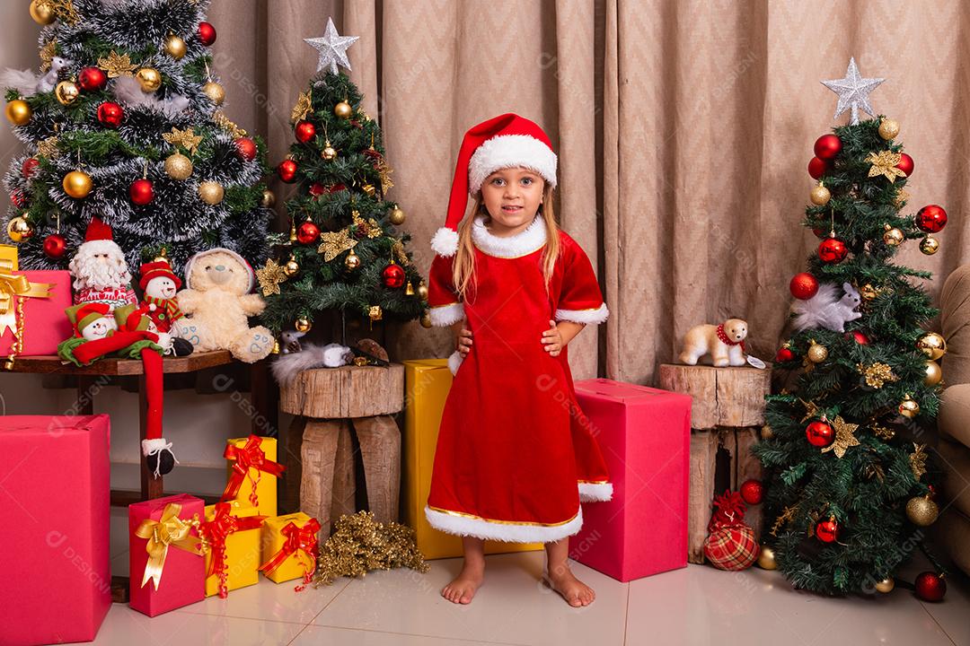 Menina caucasiana bonitinha vestida para o natal em casa. Garota em fundo de Natal vestida de noelete