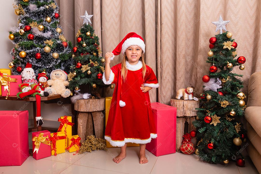Menina caucasiana bonitinha vestida para o natal em casa. Garota em fundo de Natal vestida de noelete