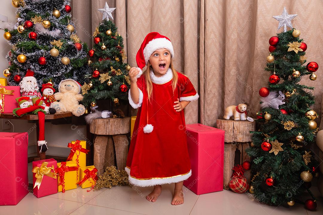 Menina caucasiana bonitinha vestida para o natal em casa. Garota em fundo de Natal vestida de noelete