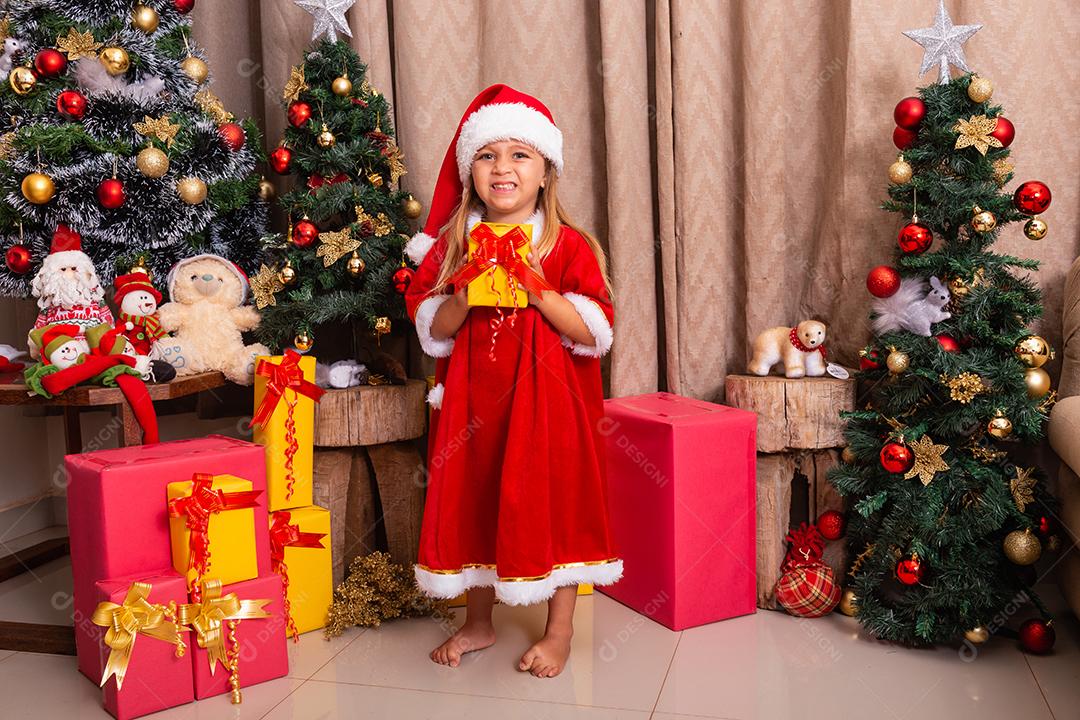 menina caucasiana bonitinha vestida para o natal em casa segurando um presente.