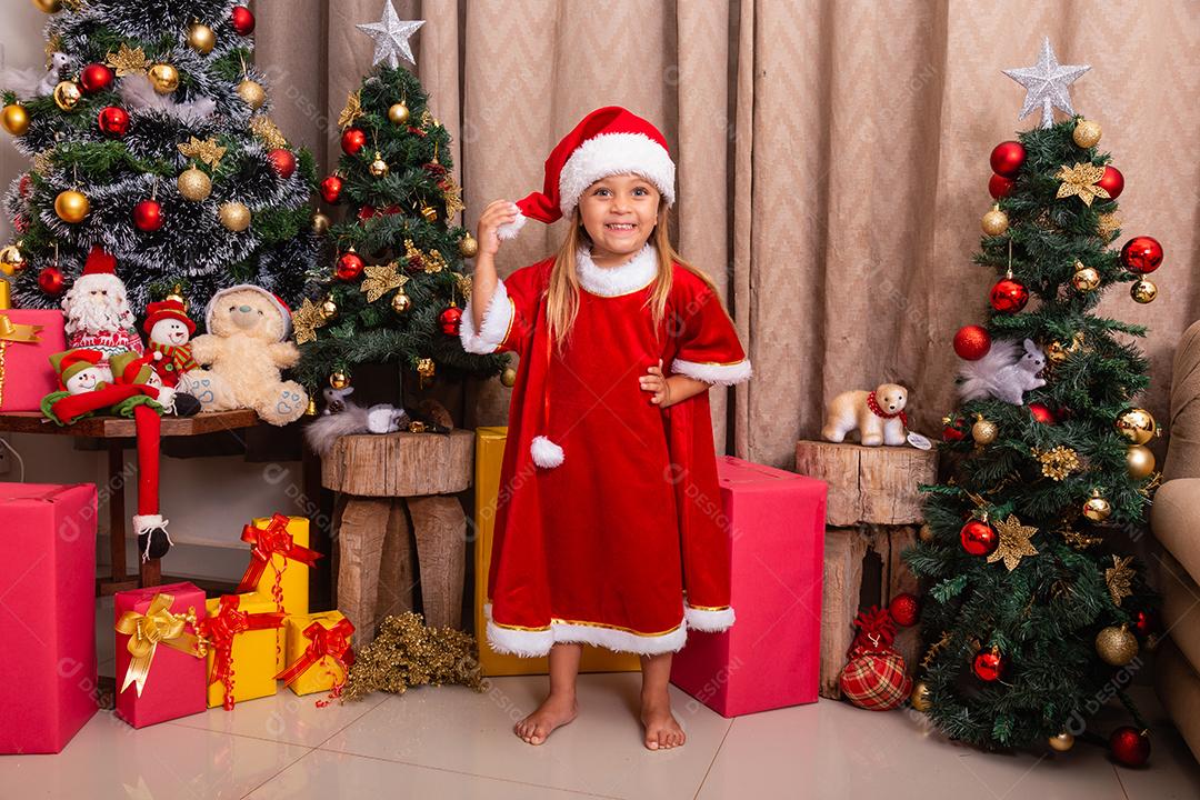 Menina caucasiana bonitinha vestida para o natal em casa. Garota em fundo de Natal vestida de noelete