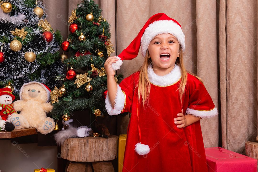 Menina caucasiana bonitinha vestida para o natal em casa. Garota em fundo de Natal vestida de noelete