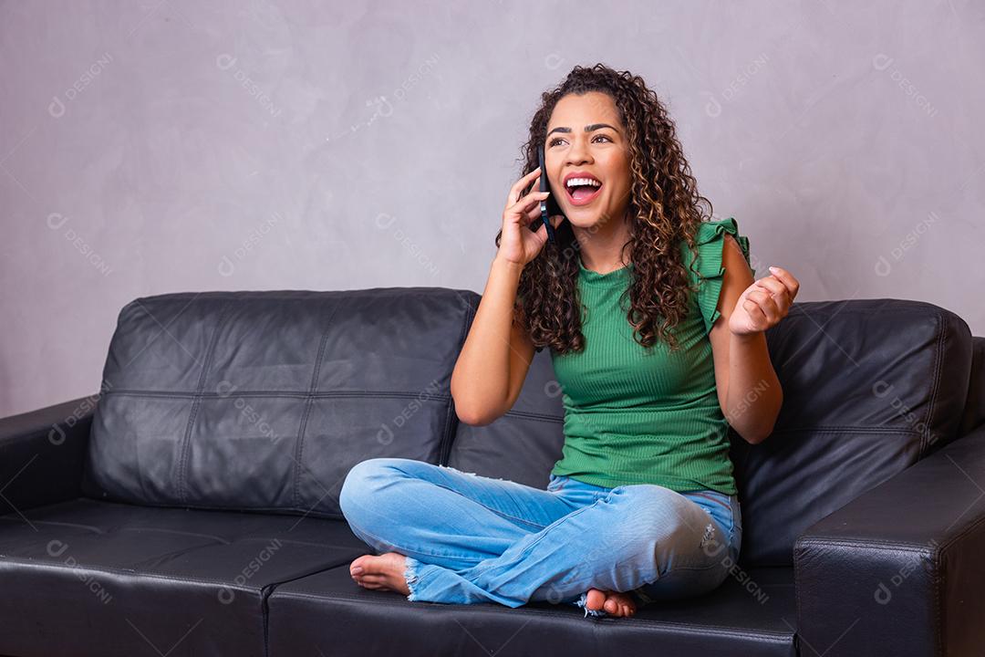 Mulher afro sentada no sofá segurando o celular com tela branca