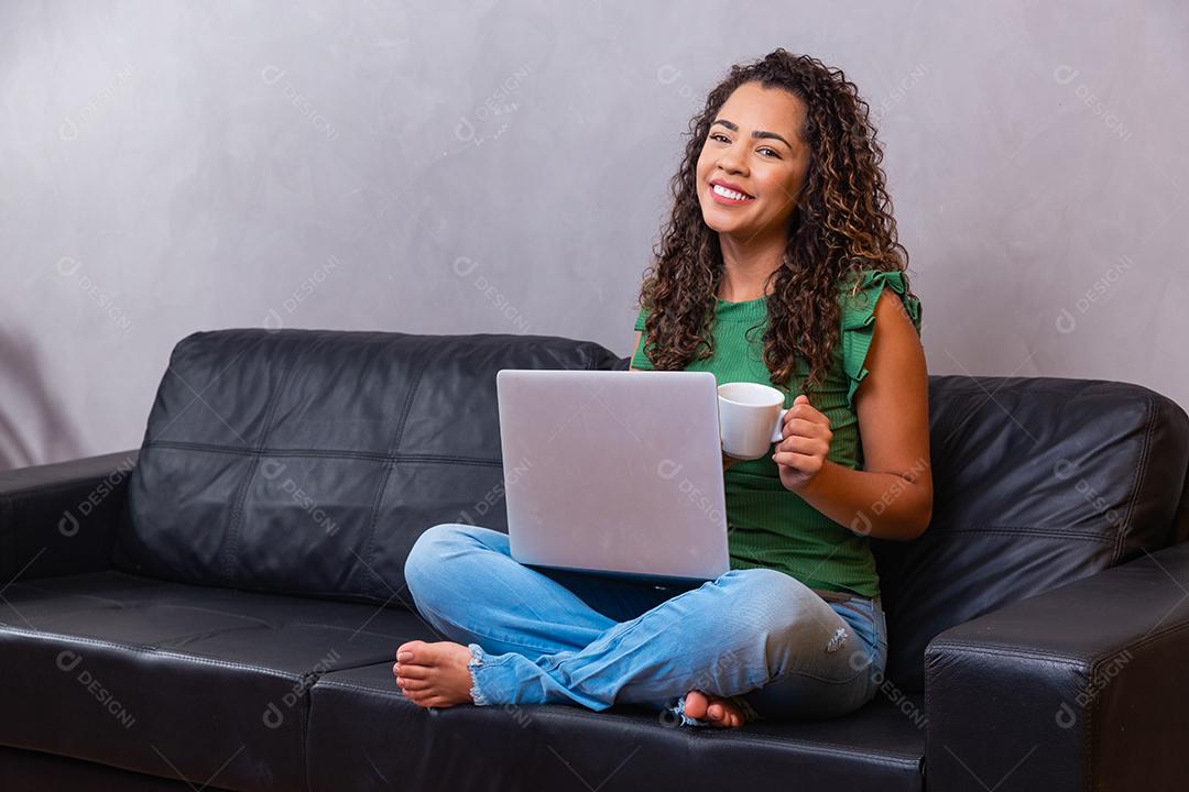 Sorrindo jovem afro usando laptop, sentado no sofá em casa, linda garota fazendo compras ou conversando