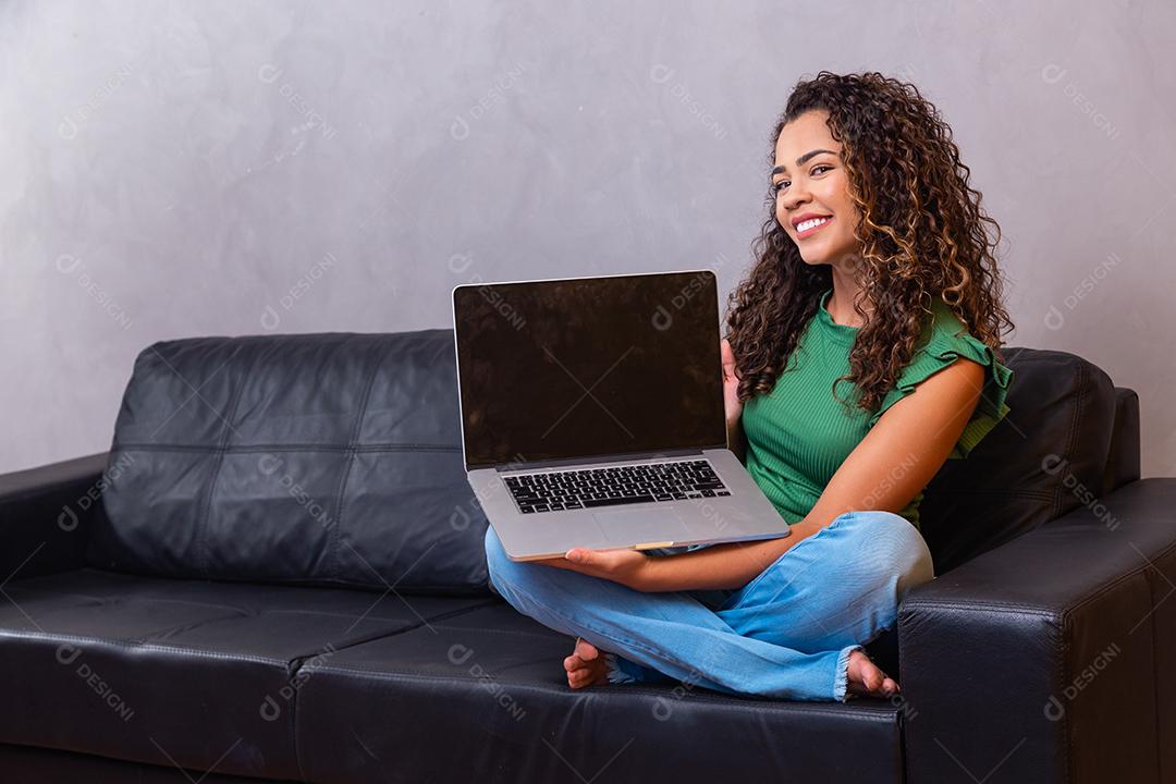 Jovem mulher sentada no sofá segurando o computador portátil pc com tela em branco vazia
