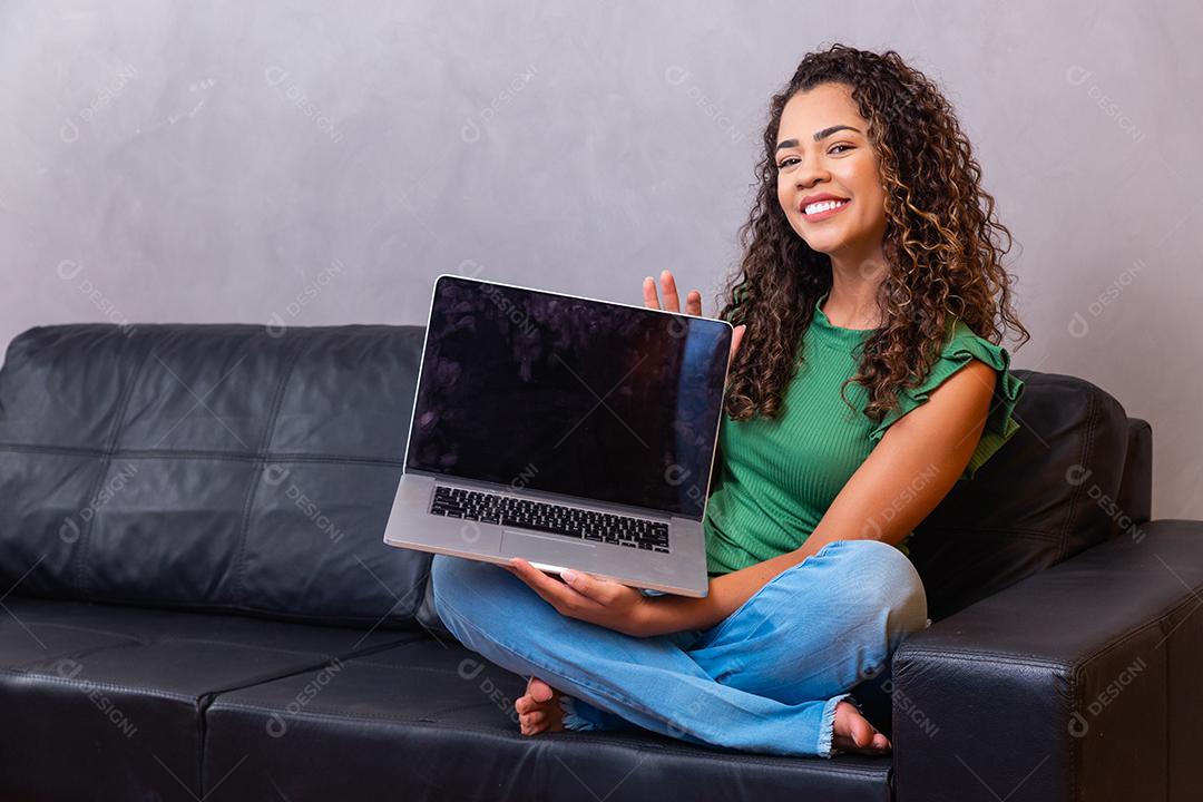 Jovem mulher sentada no sofá segurando o computador portátil pc com tela em branco vazia