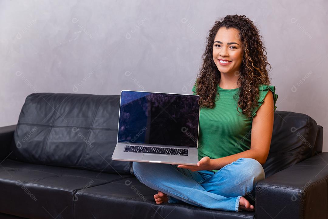 Jovem mulher sentada no sofá segurando o computador portátil pc com tela em branco vazia