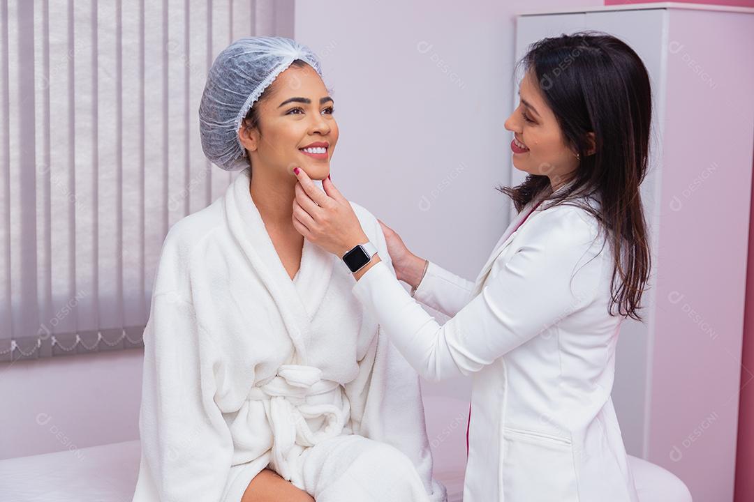 Médico ou dentista avaliando o rosto de uma linda mulher afro para tratamento estético