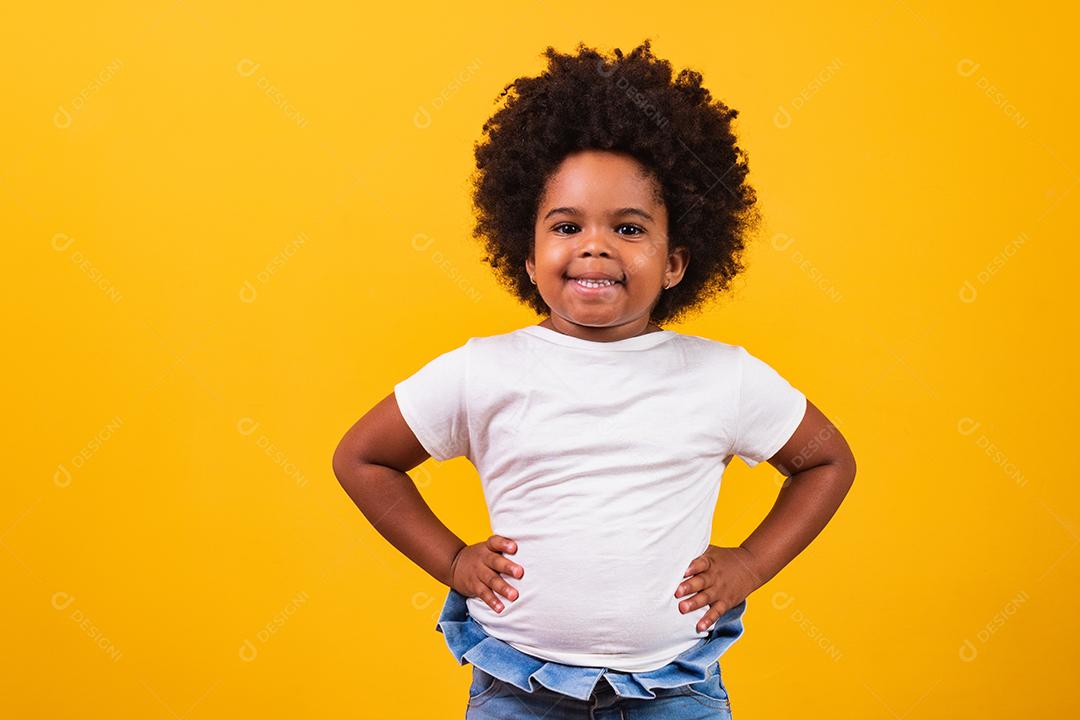 Conceito de infância e pessoas - feliz garotinha afro-americana em fundo amarelo. Menina negra com cabelo preto sorrindo.