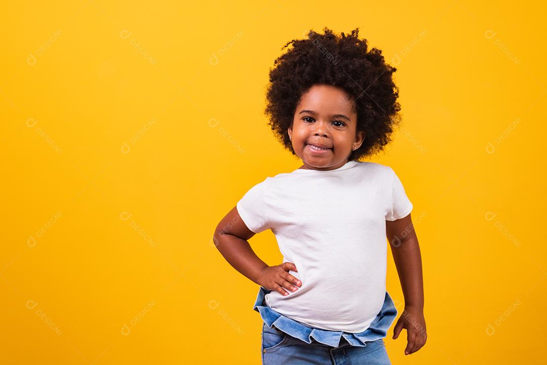 Conceito de infância e pessoas - feliz garotinha afro-americana em fundo amarelo. Menina negra com cabelo preto sorrindo.