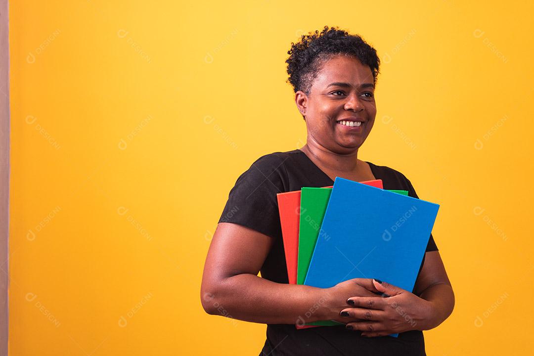 Mulher estudante madura sorrindo olhando para a câmera com espaço para texto em fundo amarelo. Mulher estudante negra madura