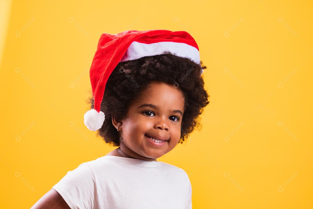 Menina afro com chapéu de Papai Noel sorrindo para o camer