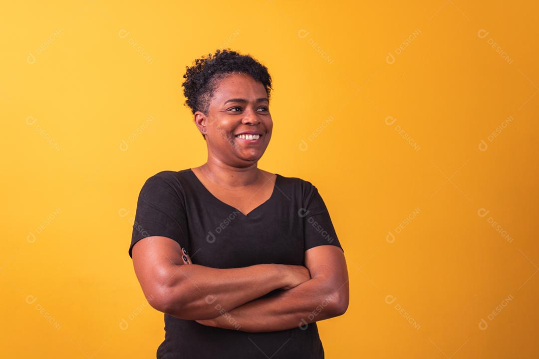 Mulher afro madura com braços cruzados em fundo amarelo