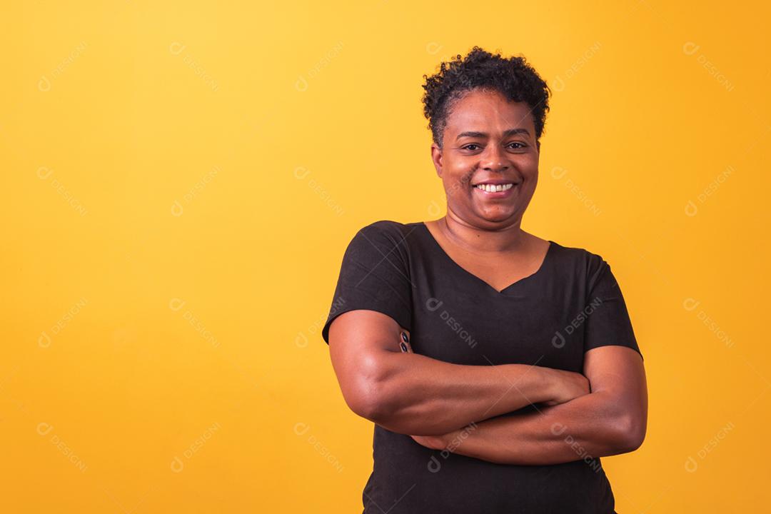 Mulher afro madura com braços cruzados em fundo amarelo