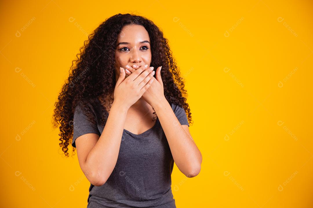 black woman on yellow background with hand on mouth, concept