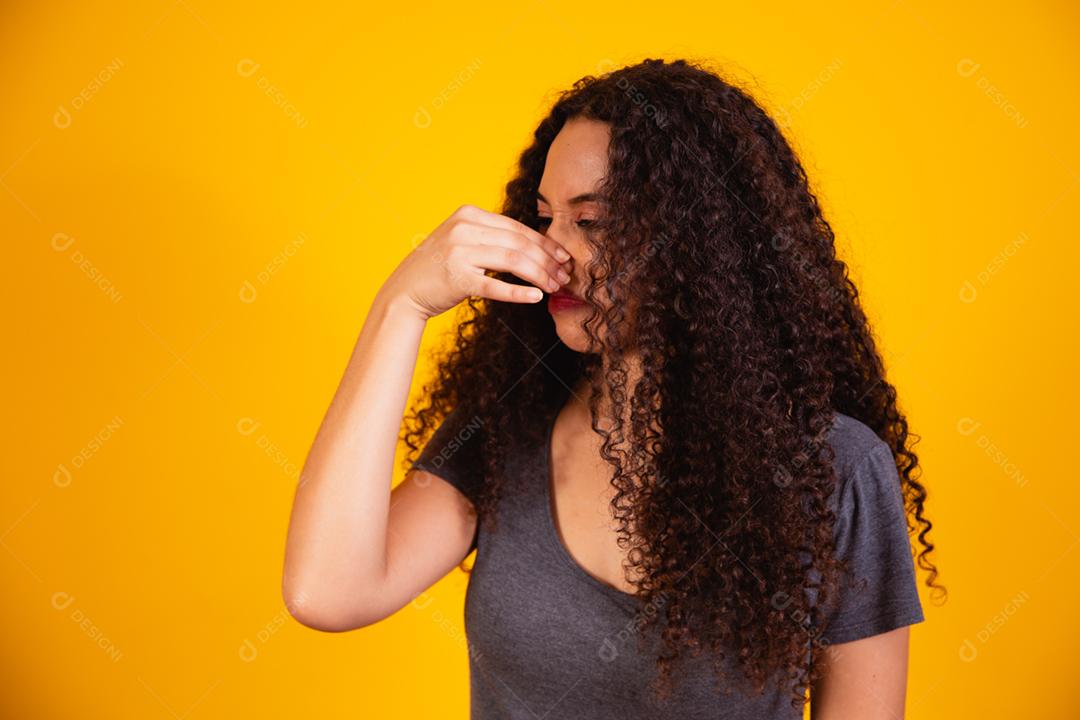mulher afro sentindo nojo, segurando o nariz para evitar cheirar um fedor