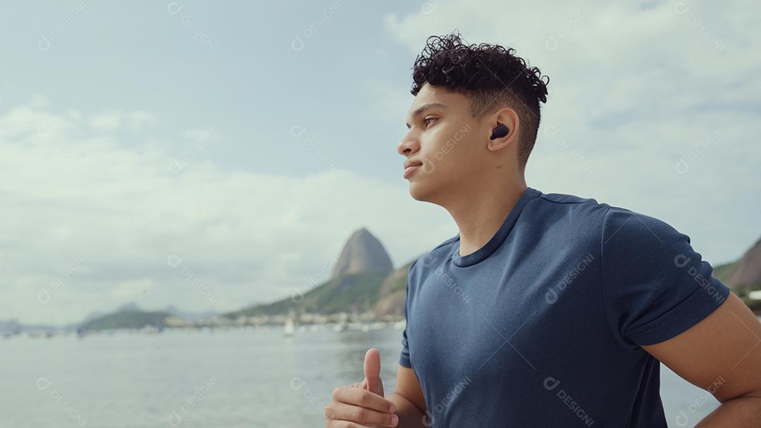 Young man running while listening to music on his headphones on the beach in Rio de Janeiro.