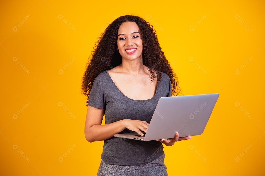 Trabalho remoto! Retrato de uma jovem afro animada segurando o laptop isolado sobre fundo amarelo