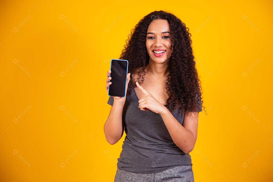 Garota afro-americana espantada apontando para a tela do telefone em branco.