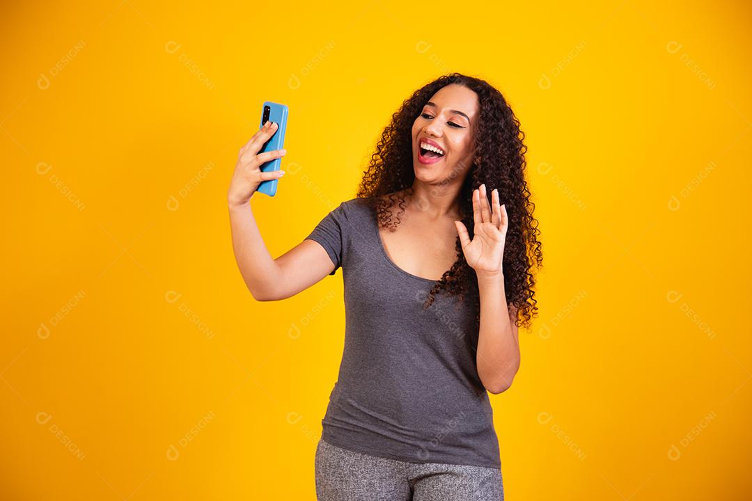 retrato de jovem afro em chamada de vídeo por telefone celular em fundo amarelo.