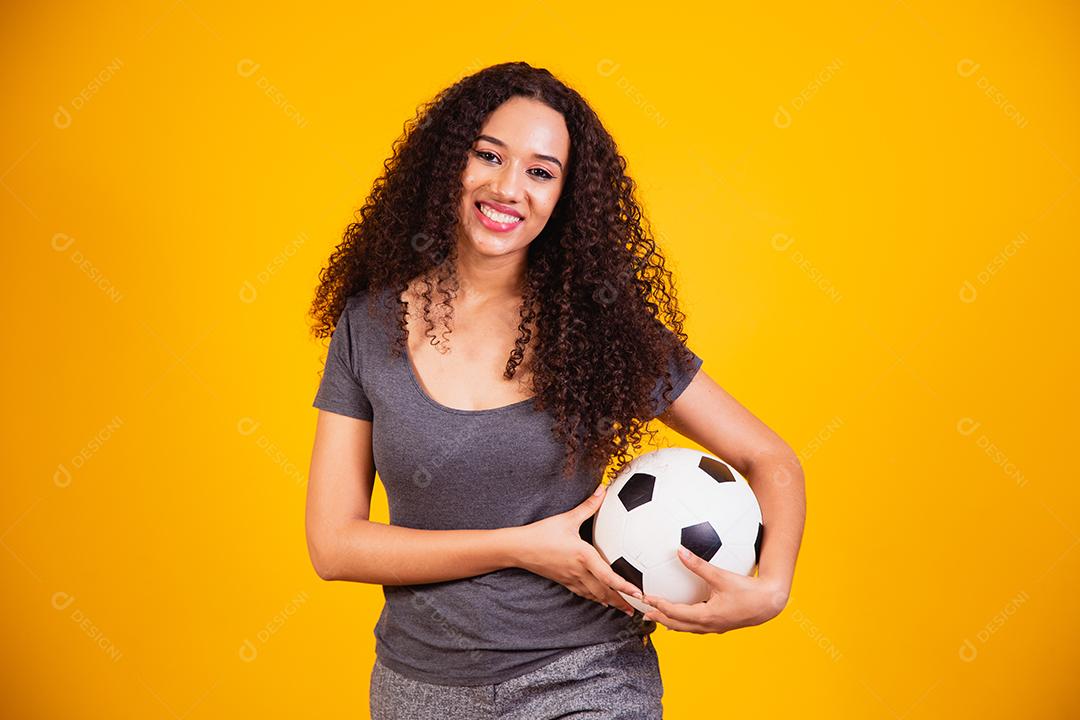 Jovem mulher afro-americana isolada em fundo amarelo com bola de futebol