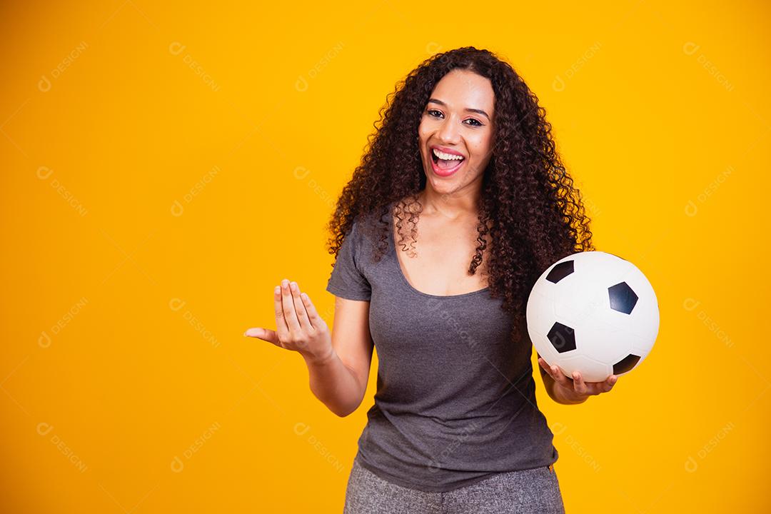 Jovem mulher afro-americana isolada em fundo amarelo com bola de futebol