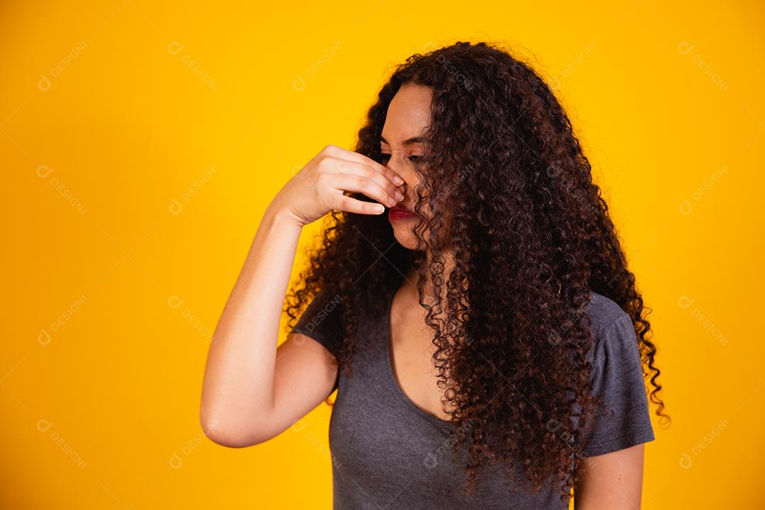 mulher afro sentindo nojo, segurando o nariz para evitar cheirar um fedor sujo e desagradável