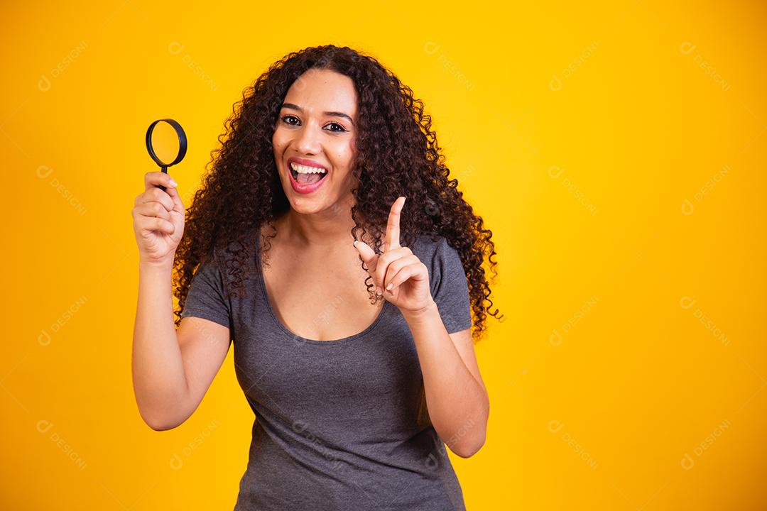 Foto de uma jovem mulher de pele escura feliz segura as mãos da lente de vidro da lupa bom humor isolado em fundo de cor amarela