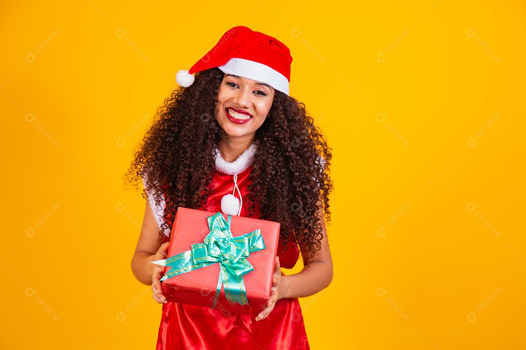 jovem noelete vestida para o natal segurando um presente em fundo amarelo.